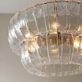 Carlwell 6 Light Pendant in brass, close-up of two-tier curved clear glass panels with illuminated bulbs and brushed brass frame.