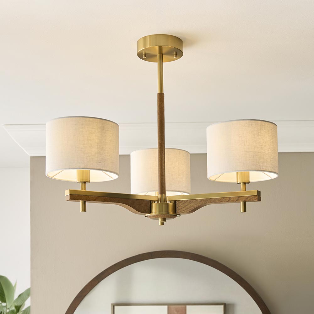 Bramwell 3 Light semi-flush ceiling light with aged brass frame, oak arms and linen drum shades, shown fitted in a room with an arched mirror below.