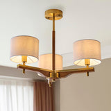 Bramwell 3-light semi-flush ceiling light with aged brass frame, oak arms and cream linen drum shades, shown fitted in a room with pale walls.