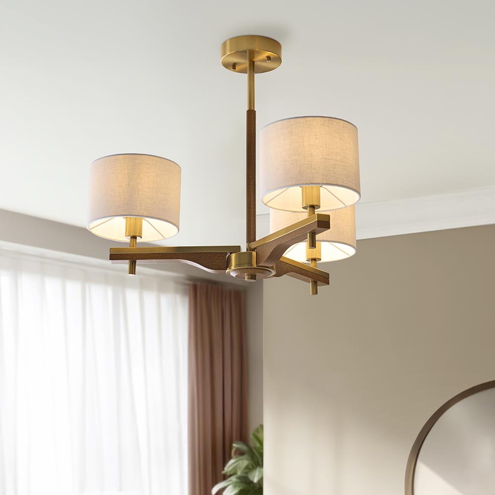 Bramwell 3-light semi-flush ceiling light with aged brass frame, oak arms and linen drum shades, shown fitted in a room with sheer curtains.