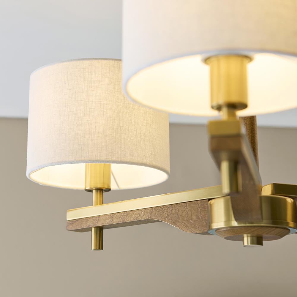 Close-up of the Bramwell 3-light semi-flush ceiling light showing aged brass arms, oak detailing, and linen drum shades illuminated from within.