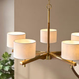 Bramwell 5 light pendant with brushed aged brass frame, oak-stained wood arms and natural linen cylinder shades, shown against a neutral wall.