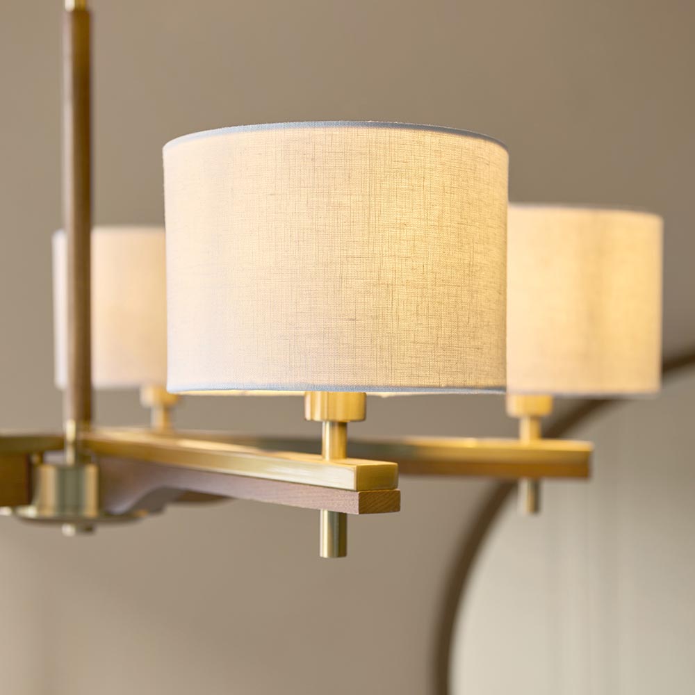 Close-up of the Bramwell 5 Light Pendant showing natural linen cylinder shades on brushed aged brass fittings with oak-stained wood detailing.