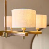 Close-up of the Bramwell 5 Light Pendant showing natural linen cylinder shades on brushed aged brass fittings with oak-stained wood detailing.