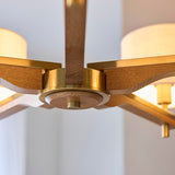 Close-up of the Bramwell 5 Light Pendant's centre hub, showing brushed brass fittings, oak-stained wood arms, and natural linen cylinder shades.