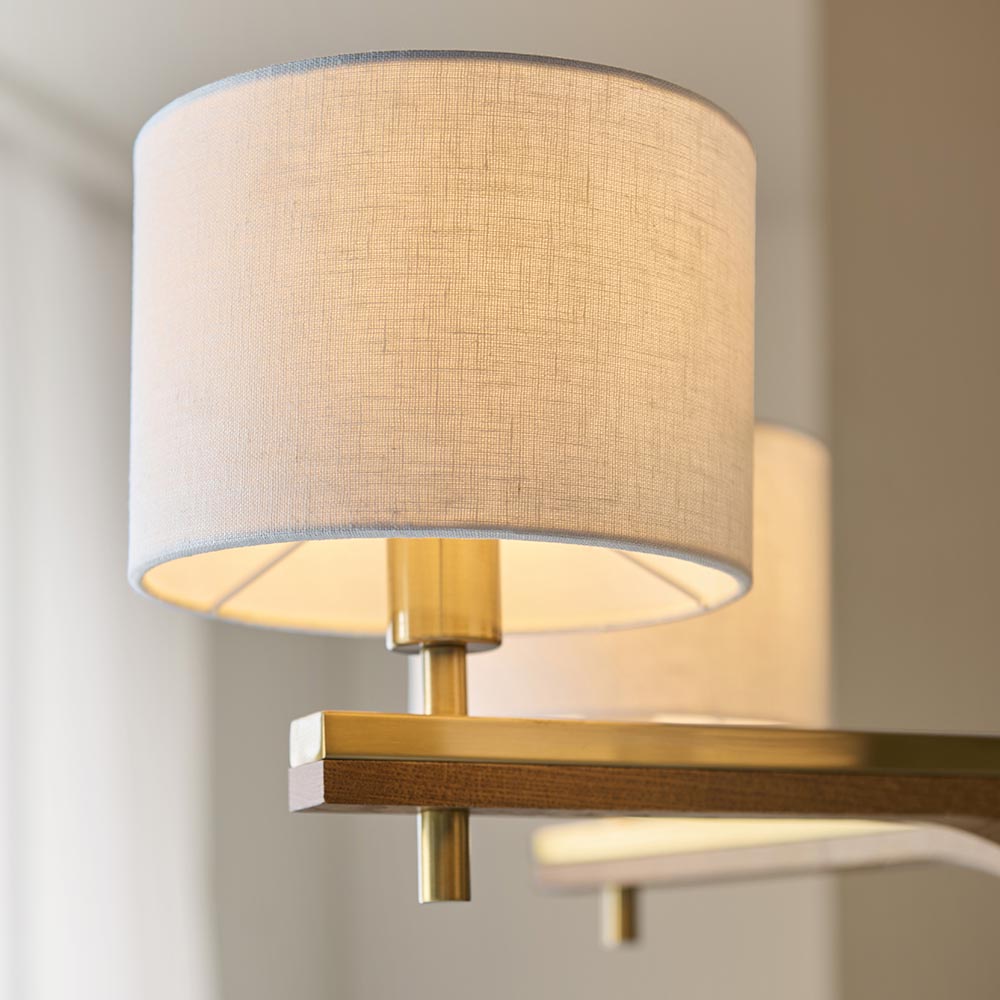 Close-up of the Bramwell 5 Light Pendant showing a natural linen cylinder shade with brushed brass fitting and wood-accented frame detail.