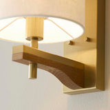 Close-up of Endon Bramwell Wall Light in antique brass, showing the brushed brass bracket, oak-stained ash wood detail, and natural faux-linen shade.