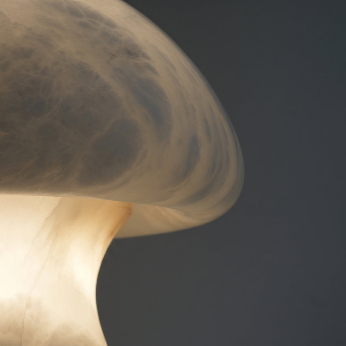 Close-up of the Morfia mushroom-form alabaster table lamp, showing veined stone dome glowing warm white against a dark background.