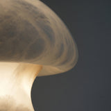 Close-up of the Morfia mushroom-shaped alabaster table lamp, showing natural stone veining glowing softly amber as light diffuses through the dome.