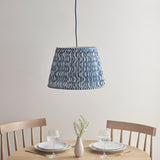 Brackmont Ripple Pendant in blue, a tapered fabric shade with wave pattern on a blue cable, hung above a wooden dining table in a light room.
