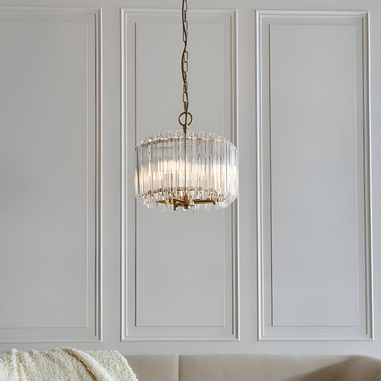 Endon Danebury 3 light pendant in brushed brass with tiered clear glass rods, suspended from a chain against a white panelled wall in a living room.