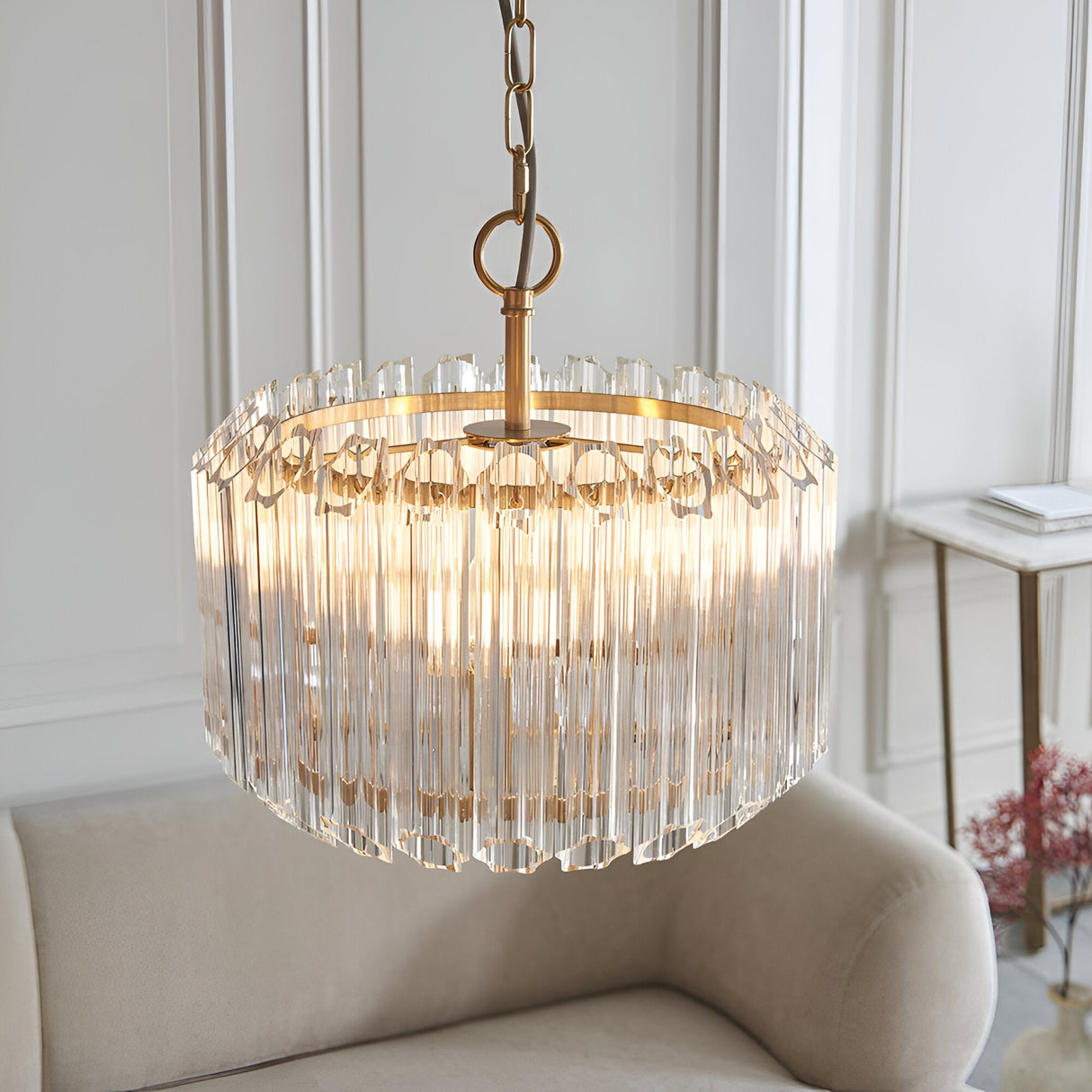 Endon Danebury 3 light pendant in brushed brass with tiered clear glass rods, suspended by chain above a cream armchair in a panelled living room.