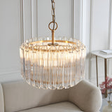 Endon Danebury 3 light pendant in brushed brass with tiered clear glass rods, suspended by chain above a cream armchair in a panelled living room.