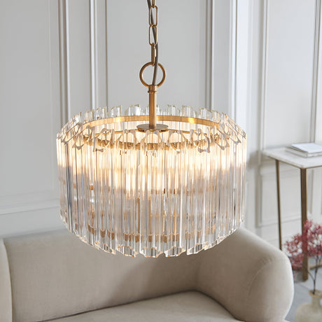 Endon Danebury 3 light pendant in brushed brass with tiered clear glass rods, suspended by chain above a cream armchair in a panelled living room.