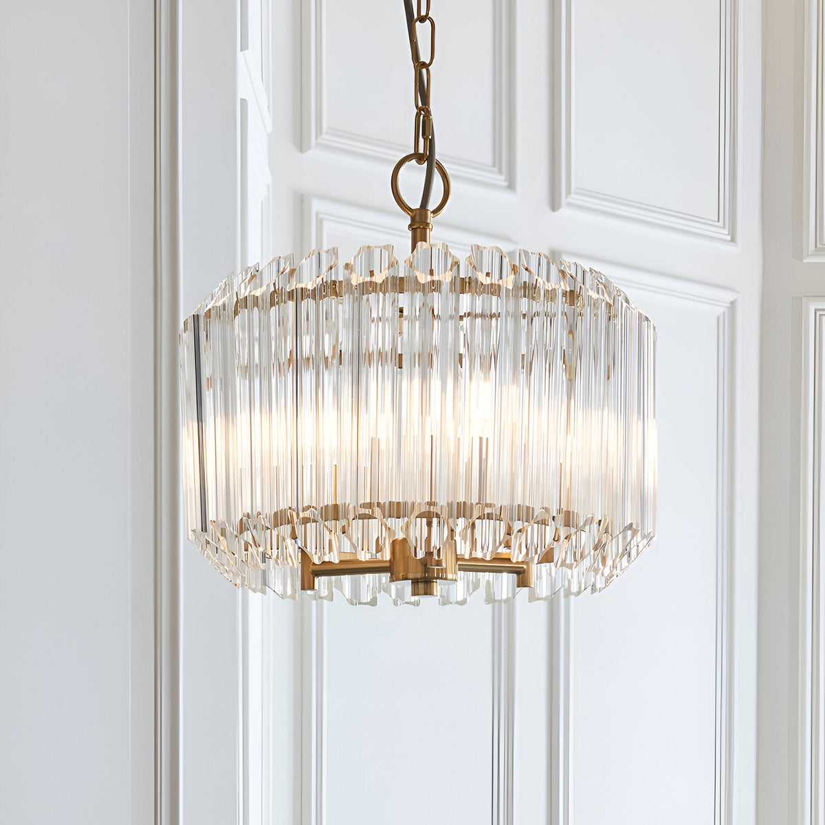 Endon Danebury 3 light pendant with tiered clear glass rods around a brushed aged brass frame, suspended from a chain against white panelled walls.