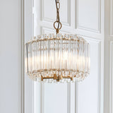 Endon Danebury 3 light pendant with tiered clear glass rods around a brushed aged brass frame, suspended from a chain against white panelled walls.