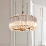 Endon Danebury 5 light pendant in aged brass with vertical clear crystal rods forming a drum shade, suspended from a chain against panelled walls.