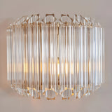 Endon Danebury wall light with faceted clear glass rods on a brushed aged brass frame, illuminated against a pale wall.