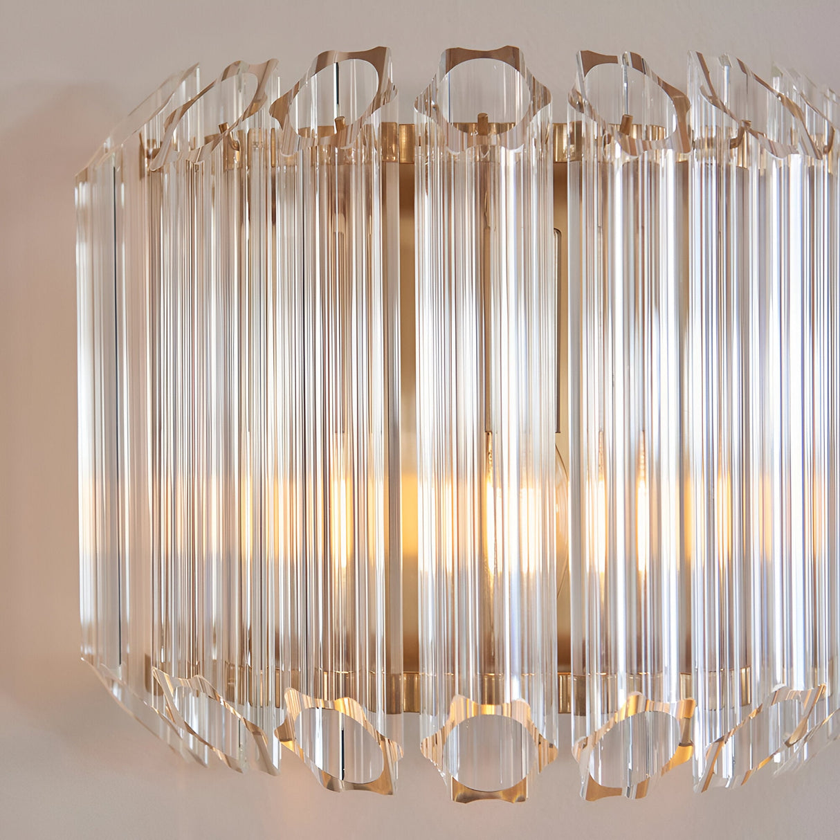 Endon Danebury wall light with faceted clear glass rods on a brushed aged brass frame, illuminated against a pale wall.