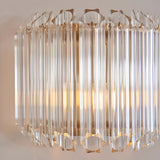 Endon Danebury wall light with faceted clear glass rods on a brushed aged brass frame, illuminated against a pale wall.