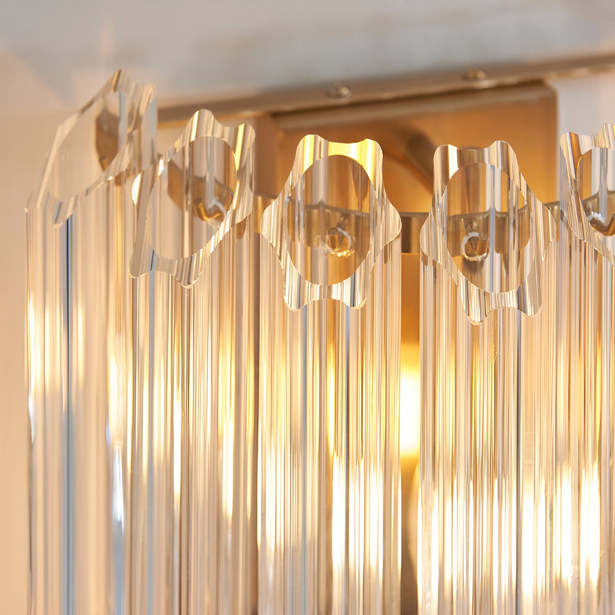 Close-up of the Endon Danebury wall light showing faceted clear glass rods set into a brushed aged brass frame with a warm glow behind.