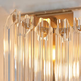Close-up of the Endon Danebury wall light showing faceted clear glass rods set into a brushed aged brass frame with a warm glow behind.