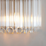 Close-up of Endon Danebury wall light showing faceted clear glass rods illuminated by a warm E14 bulb within a brushed aged brass frame.