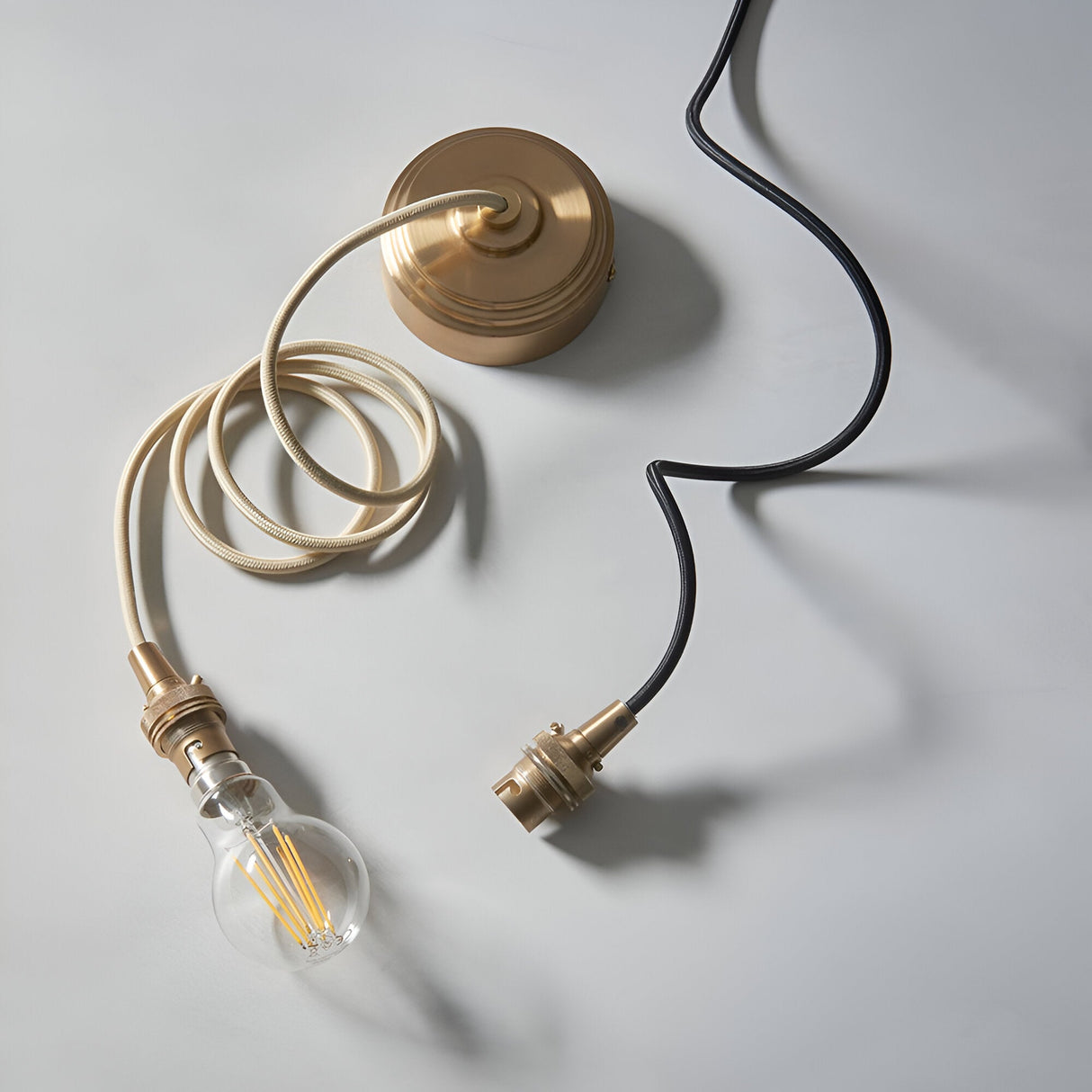 Endon Brackmont Flex Set in brushed brass with B22 lampholder, braided fabric cable, ceiling rose and filament bulb laid on a pale background.