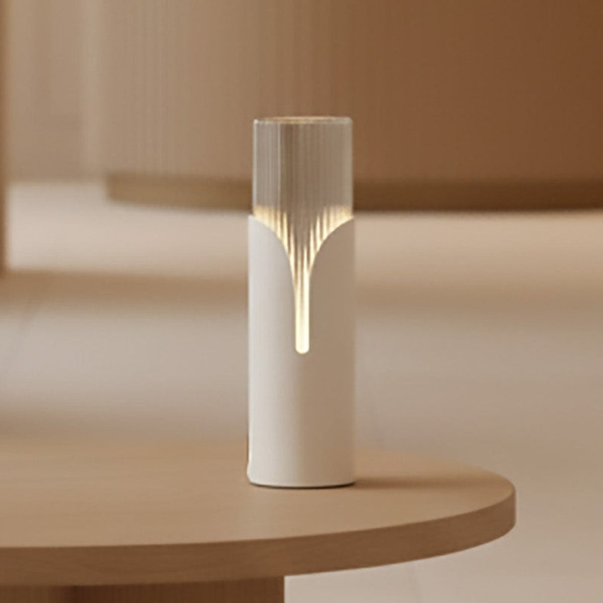 Bisel Cylinder Ribbed Glass Table Lamp in matt white, glowing on a rounded wooden table edge with a petal-shaped cutaway revealing a soft downward light line.