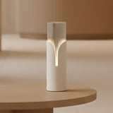 Bisel Cylinder Ribbed Glass Table Lamp in matt white, glowing on a rounded wooden table edge with a petal-shaped cutaway revealing a soft downward light line.