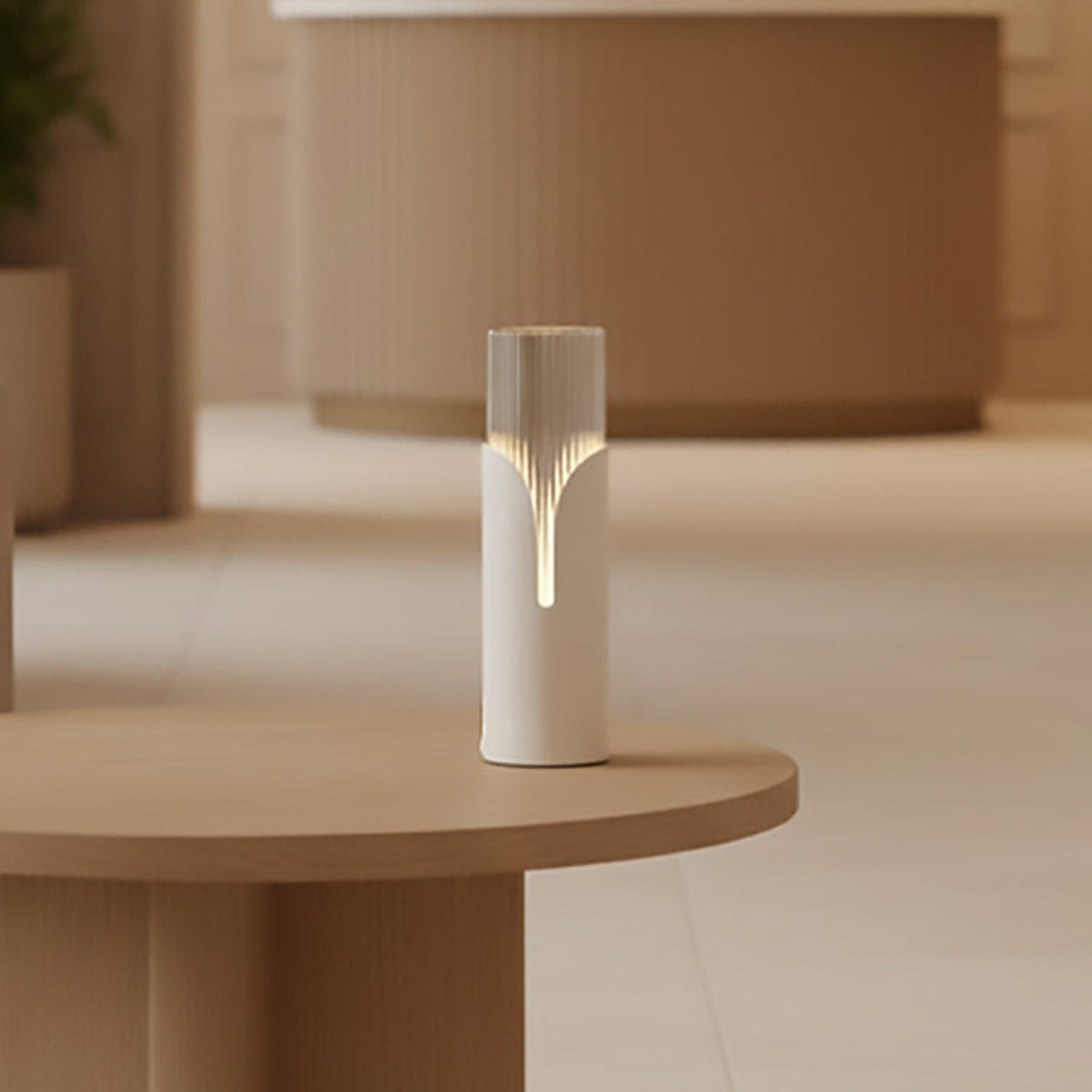 Bisel Cylinder Ribbed Glass Table Lamp in matt white, with a tapering cut-away sleeve revealing softly lit fluted glass, shown on a wooden side table in a warm-toned room.