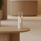 Bisel Cylinder Ribbed Glass Table Lamp in matt white, with a tapering cut-away sleeve revealing softly lit fluted glass, shown on a wooden side table in a warm-toned room.