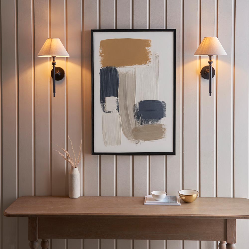 Endon Caldmere wall lights in black with tapered natural linen shades, mounted as a symmetrical pair on panelled wall above a wooden console with abstract art.