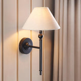 Endon Caldmere wall light in matt black with tapered natural linen shade, mounted on a panelled wall beside soft beige curtains.