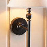 Close-up of the Endon Caldmere wall light's matt black circular backplate and upright stem with ball detail, beneath a natural linen shade.