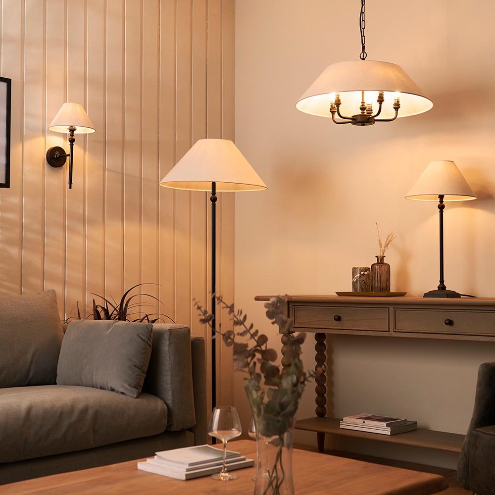 Endon Caldmere wall light in black with tapered natural linen shade, shown lit beside a floor lamp, table lamp and pendant in a warm living room.