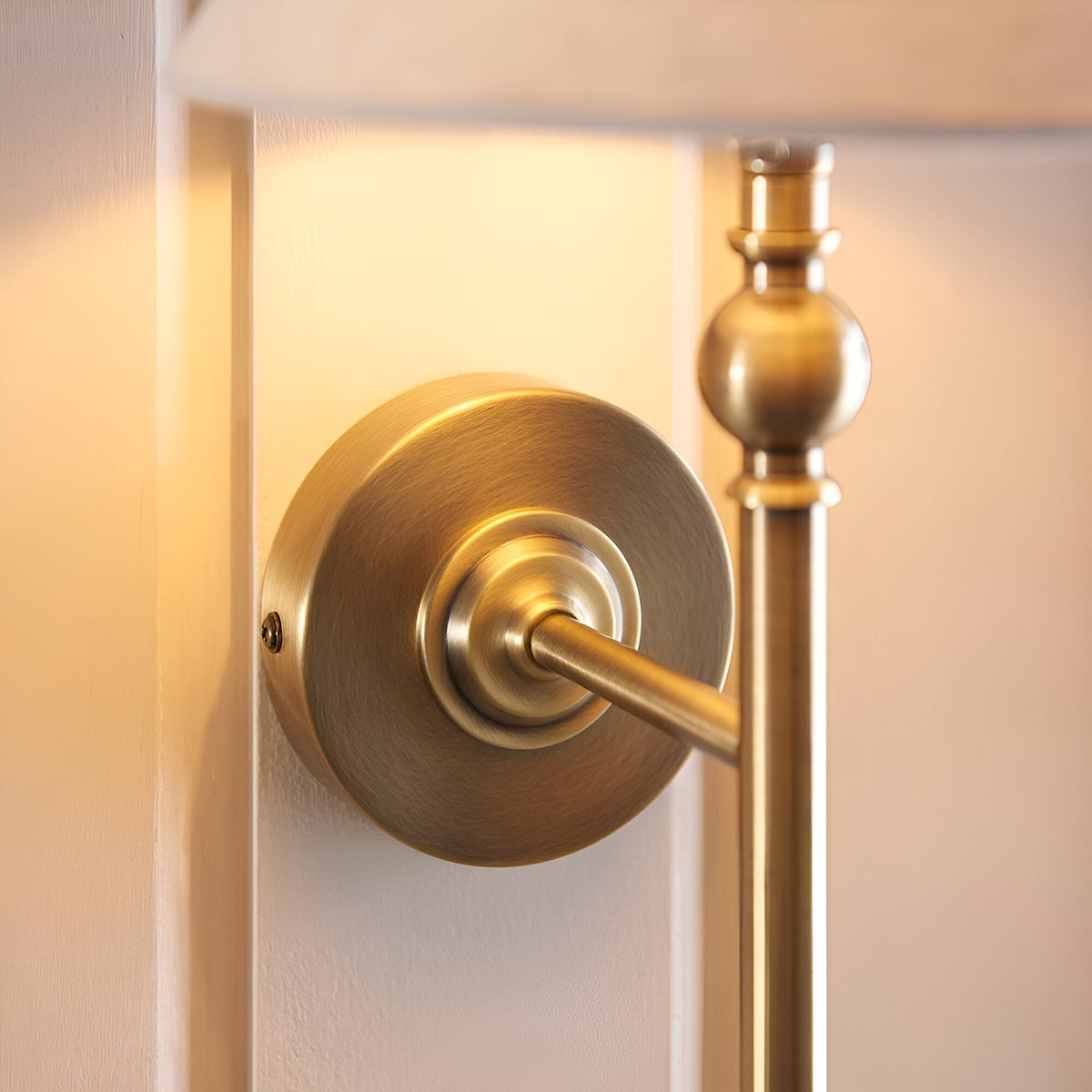 Close-up of the Endon Caldmere wall light's antique brass backplate and turned stem detail, mounted on a pale wall beneath the fabric shade.
