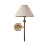 Endon Caldmere wall light in antique brass with an upright stem, ball detail and tapered natural linen shade, shown on a plain white background.