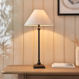 Endon Caldmont table lamp with slim turned matt black metal column and tapered natural linen shade, styled on a wood console beside framed art.