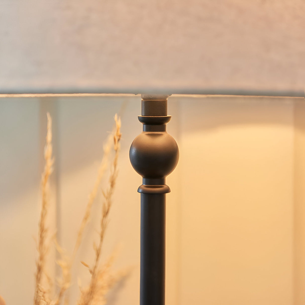 Close-up of Endon Caldmont table lamp showing turned matt black metal column with ball detail beneath a natural linen shade, styled with dried grasses.