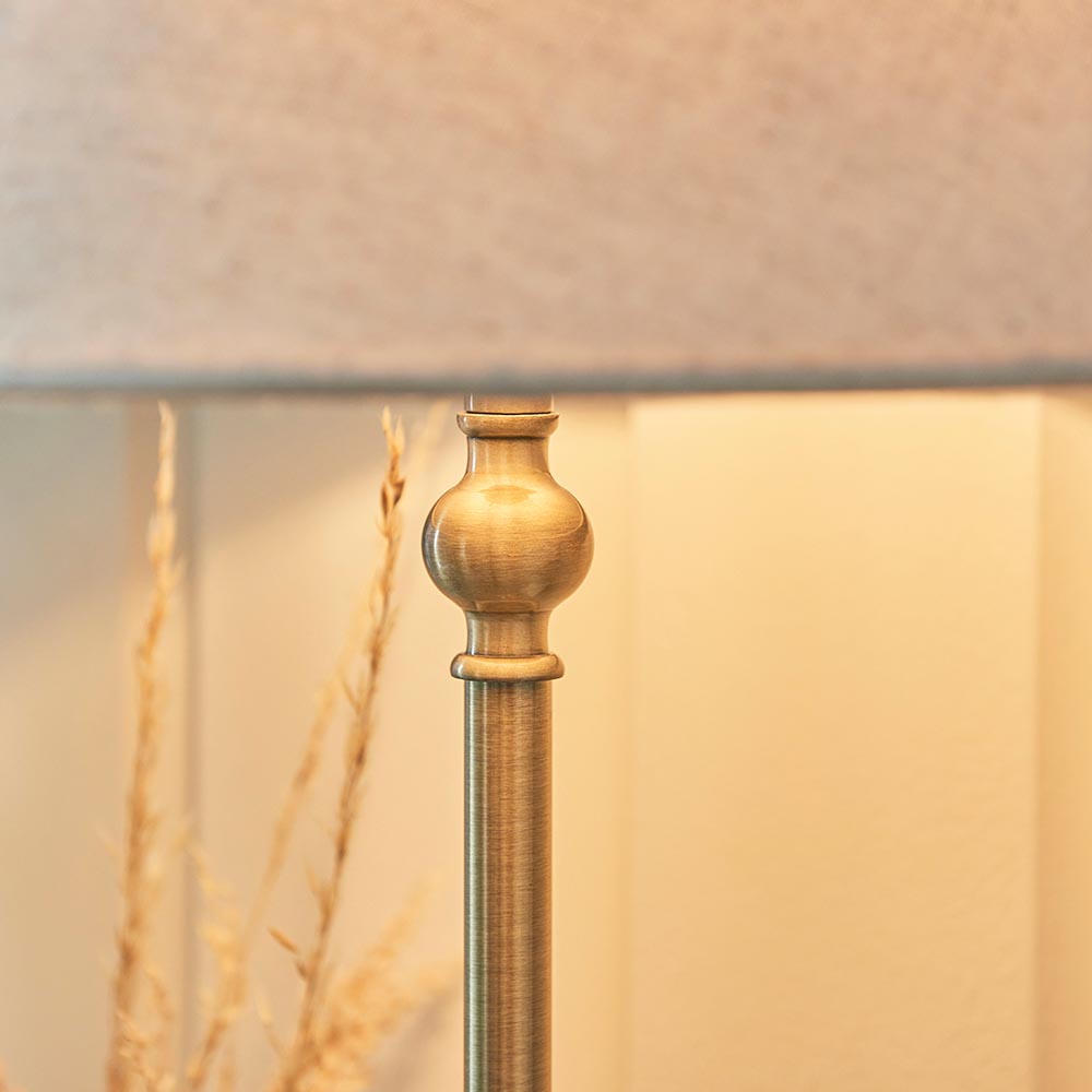Close-up of the Caldmont Table Lamp's brass turned metal column with ball detail, beneath a natural linen tapered shade, set against a warm-toned room backdrop.