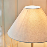 Caldmont Table Lamp with tapered natural linen shade and slim brass turned metal column, close-up view against a soft neutral background.