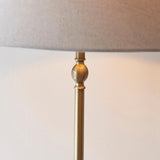 Close-up of the Endon Caldmere floor lamp's antique brass stem with decorative ball detail beneath a natural linen tapered shade.