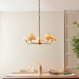 Caldmere 5 light large pendant with tapered natural linen shades on a brass finish frame and chain, shown above a dining table in a neutral room.