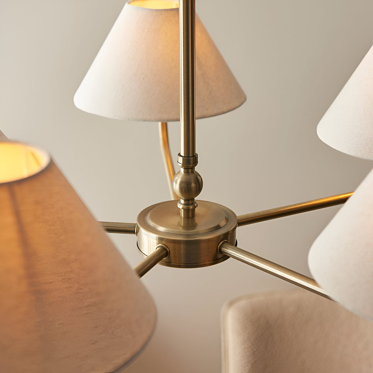 Close-up of the Caldmere 5 Light Large Pendant's brass central hub with radiating arms and tapered natural fabric shades, set against a light background.