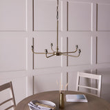 Caldmere 5 Light Large Pendant in brass, five curved arms radiating from a central rod, shown bare without shades in a dining room with panelled wall.