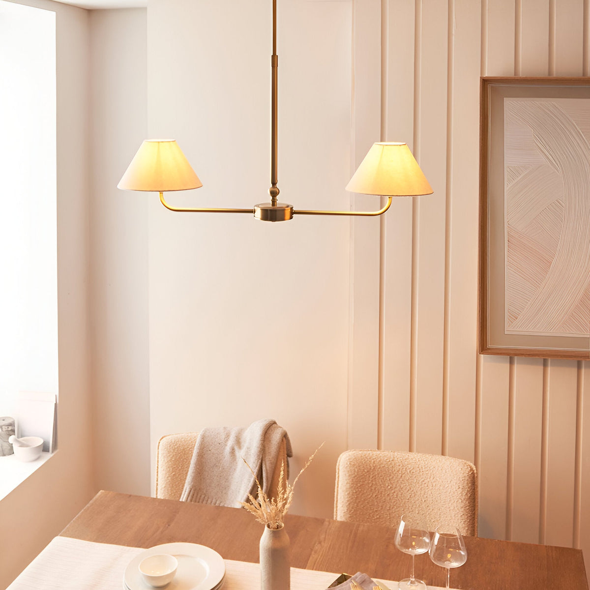 Caldmere 2 Light Pendant in brass with tapered natural linen shades on a linear bar, shown above a dining table in a light neutral room.