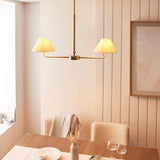 Caldmere 2 Light Pendant in brass with tapered natural linen shades on a linear bar, shown above a dining table in a light neutral room.