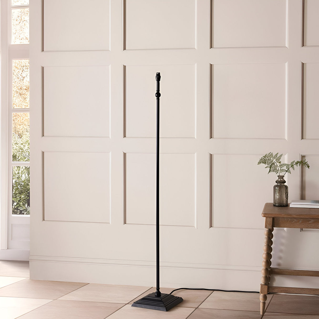 Caldmere Ikat Floor Lamp in Natural, shown without shade, featuring a slim matt black metal stem on a square stepped base, styled in a hallway.