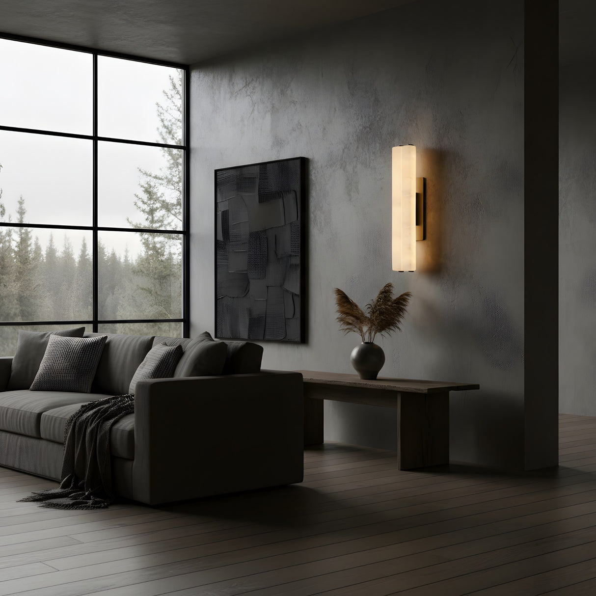 A modern living room features a gray sofa, neutral pillows, textured wall, minimalist painting, wooden bench with dried grass vase, the Selvara LED Large Alabaster Double Wall Light in Matte Black & Soft White softly glowing, and large windows with a view of trees.